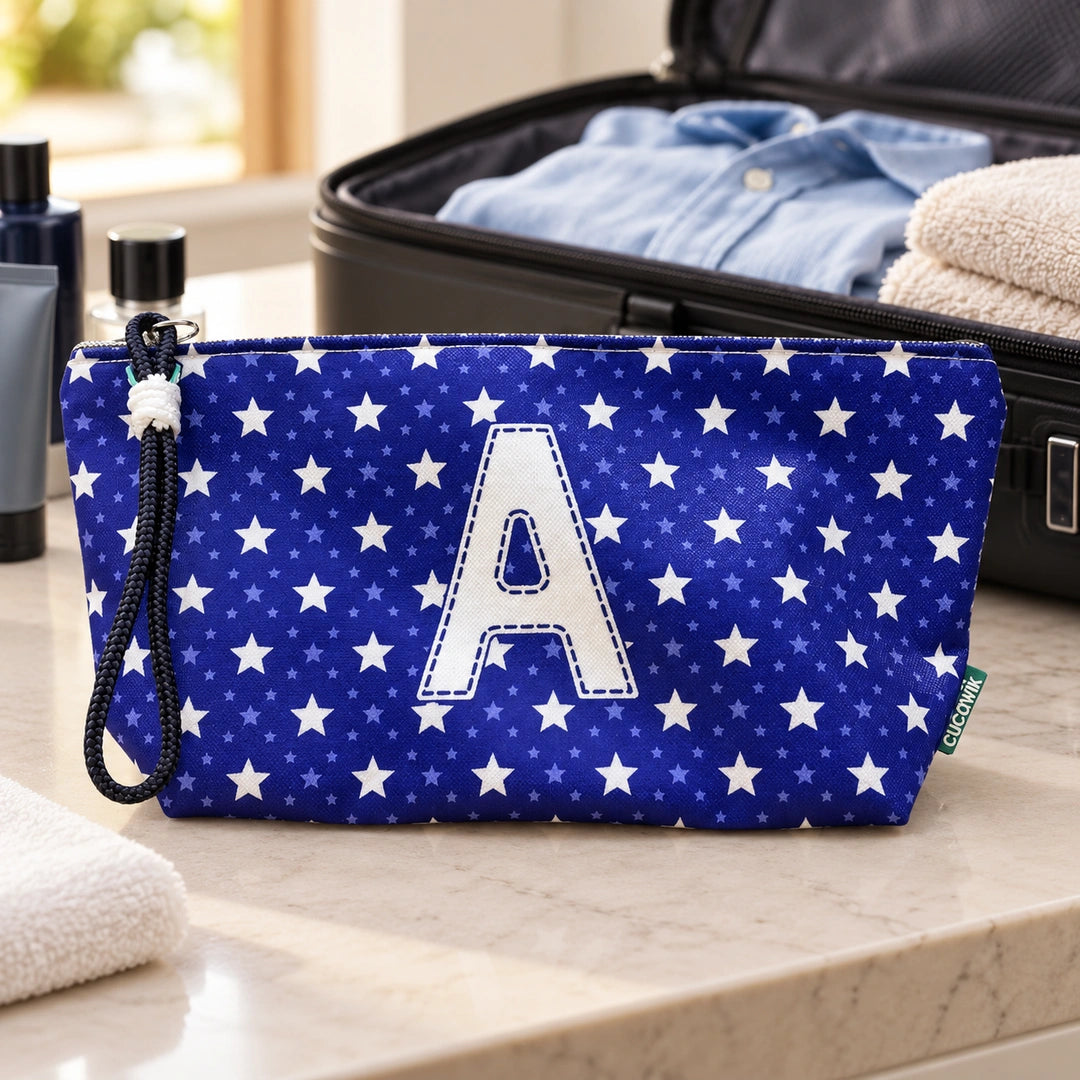 Bolsa Alex azul com letra A fechada num cenário de viagem com mala, roupa e artigos de higiene masculina.