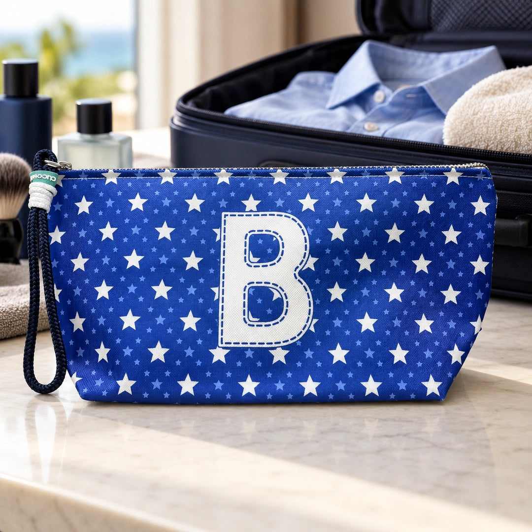 Bolsa Alex azul com letra B fechada num cenário de viagem com mala, roupa e artigos de higiene masculina.