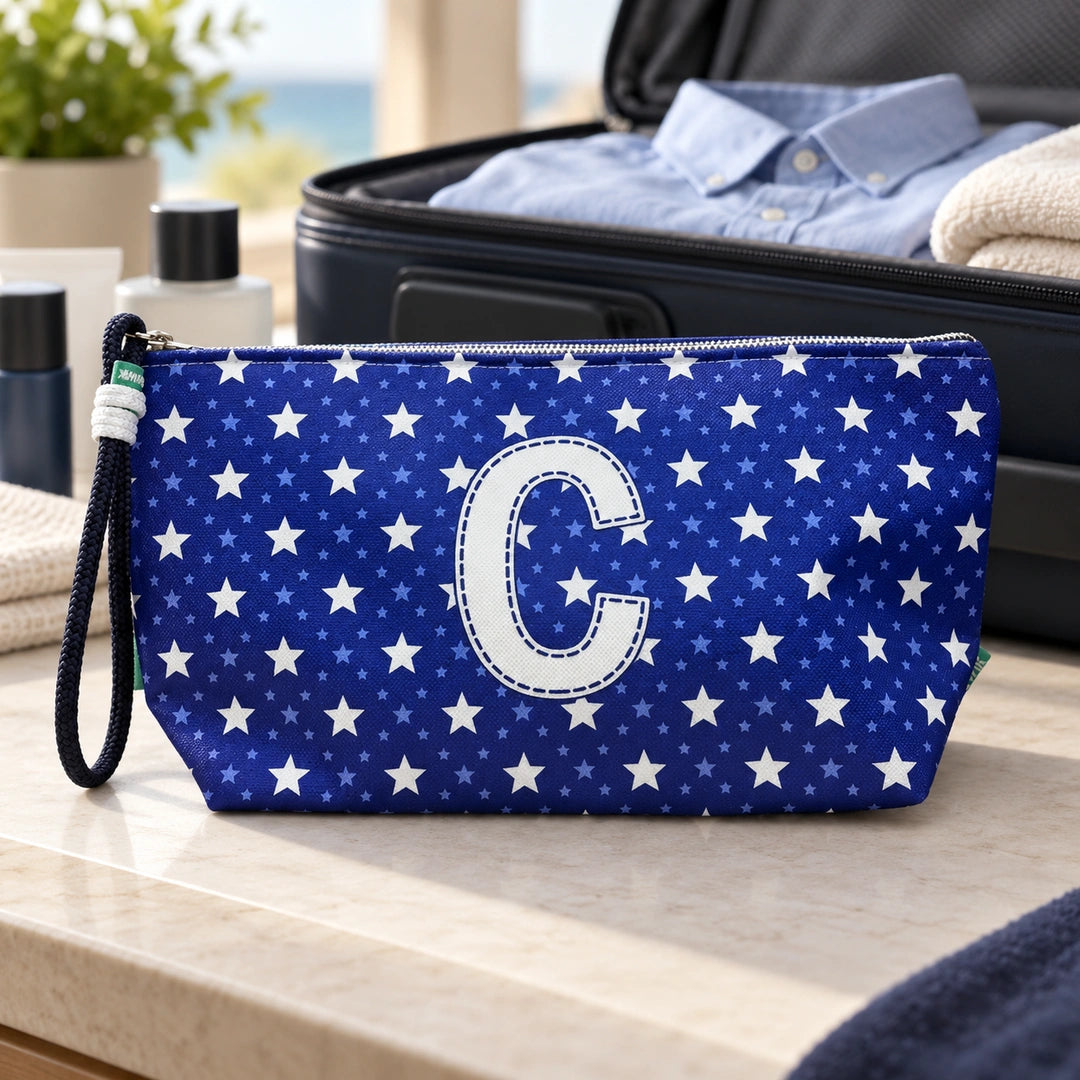 Bolsa Alex azul com letra C fechada num cenário de viagem com mala, roupa e artigos de higiene masculina.