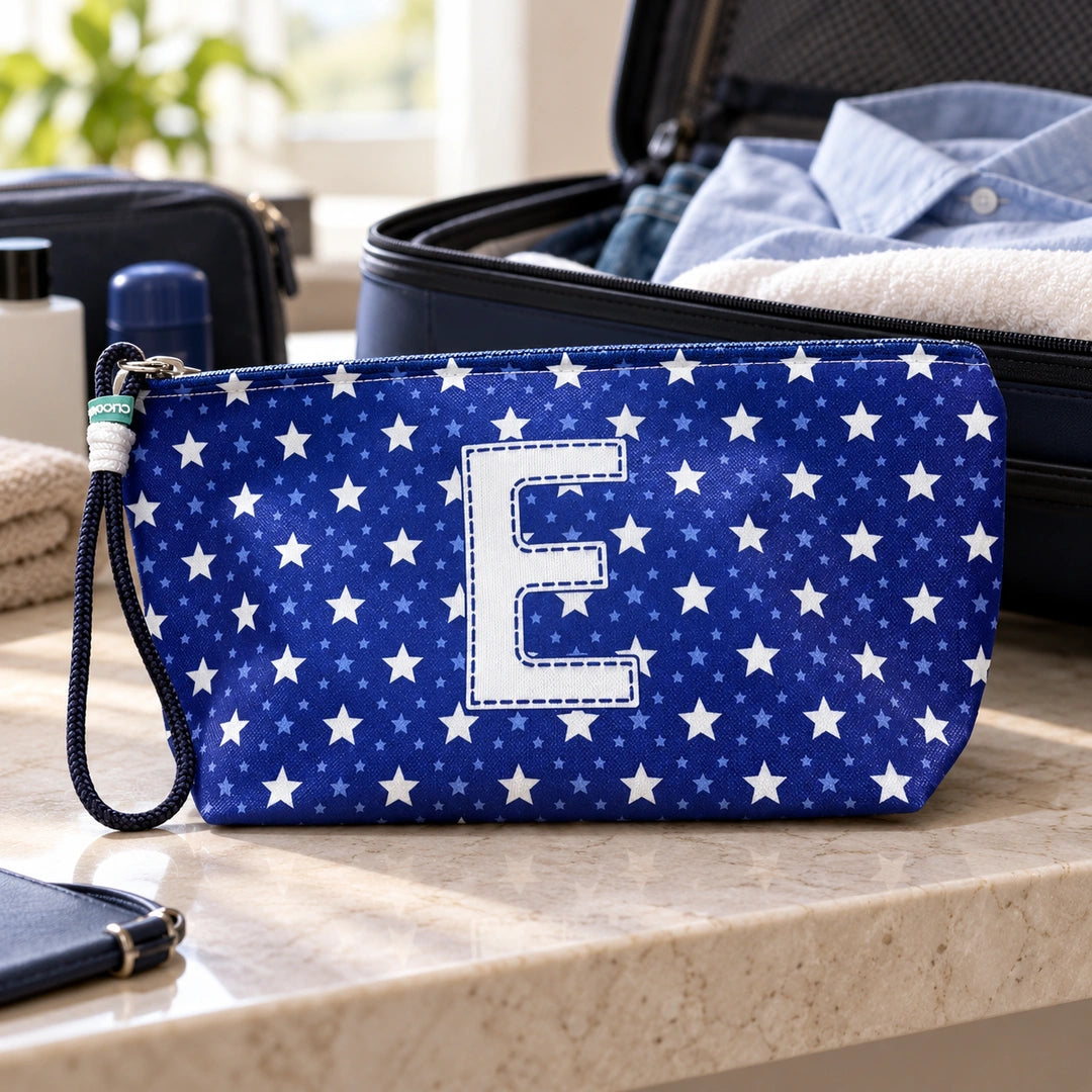Bolsa Alex azul com letra E fechada num cenário de viagem com mala, roupa e artigos de higiene masculina.