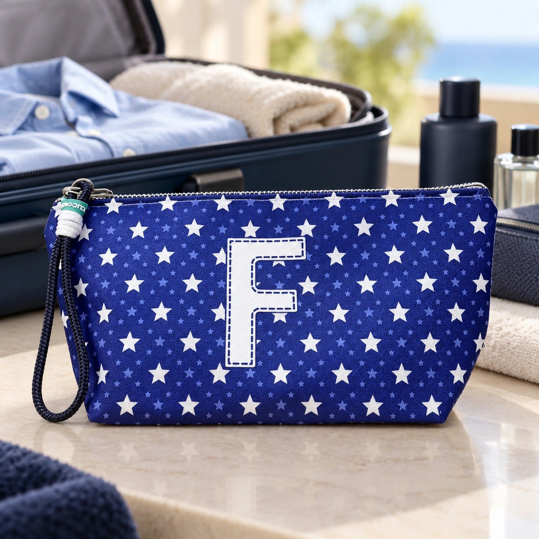 Bolsa Alex azul com letra F fechada num cenário de viagem com mala, roupa e artigos de higiene masculina.