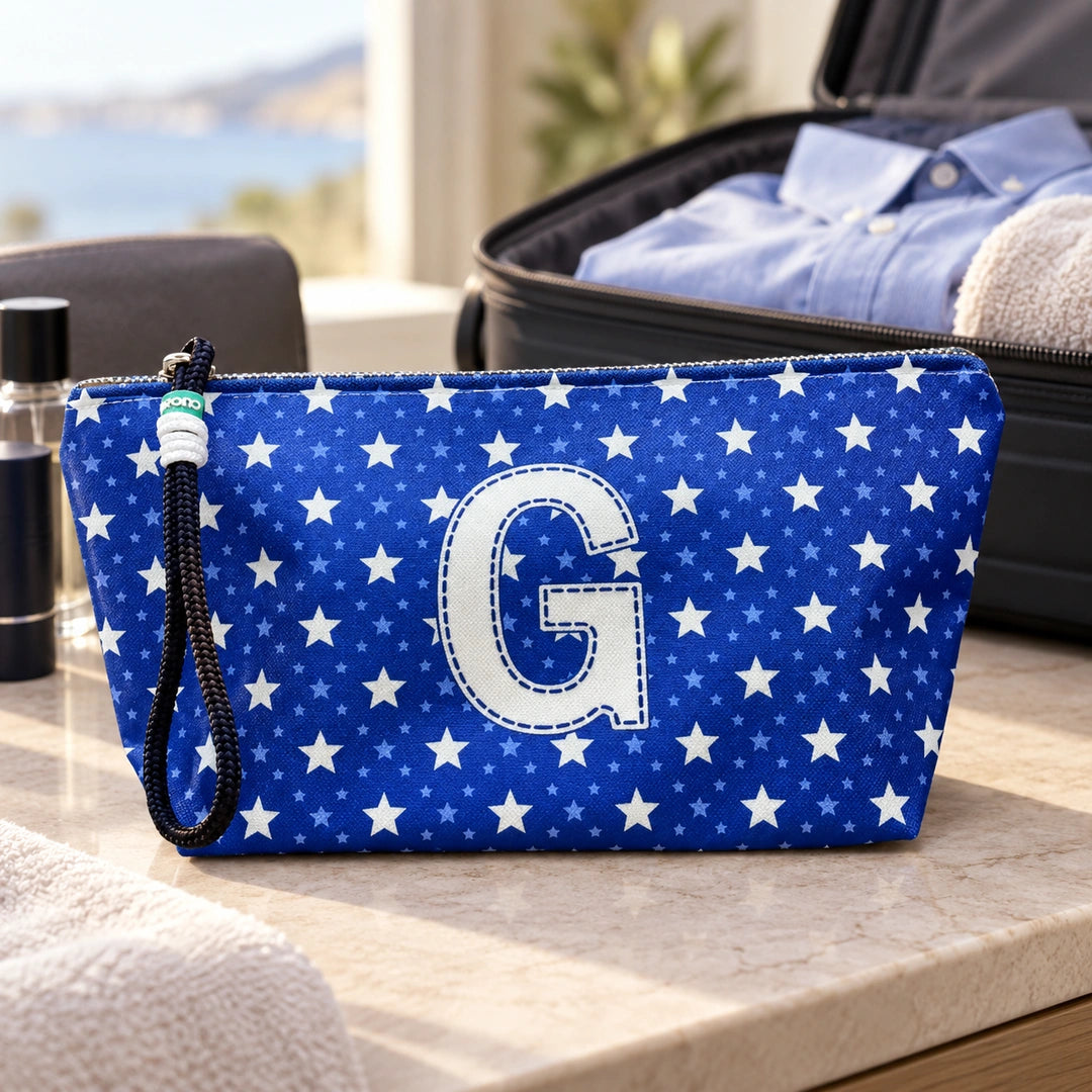 Bolsa Alex azul com letra G fechada num cenário de viagem com mala, roupa e artigos de higiene masculina.