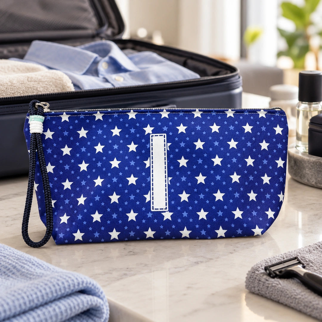 Bolsa Alex azul com letra I fechada num cenário de viagem com mala, roupa e artigos de higiene masculina.