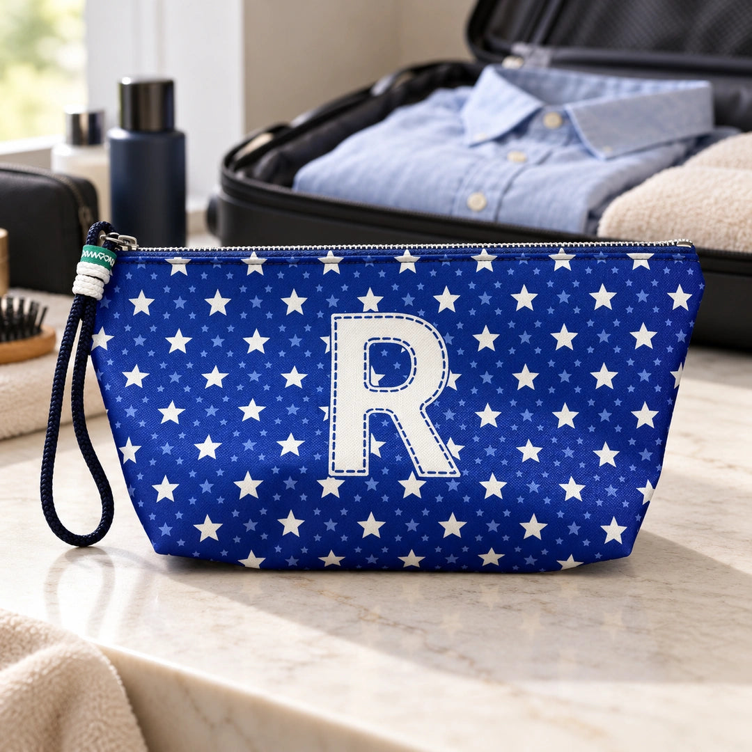 Bolsa Alex azul com letra R fechada num cenário de viagem com mala, roupa e artigos de higiene masculina.
