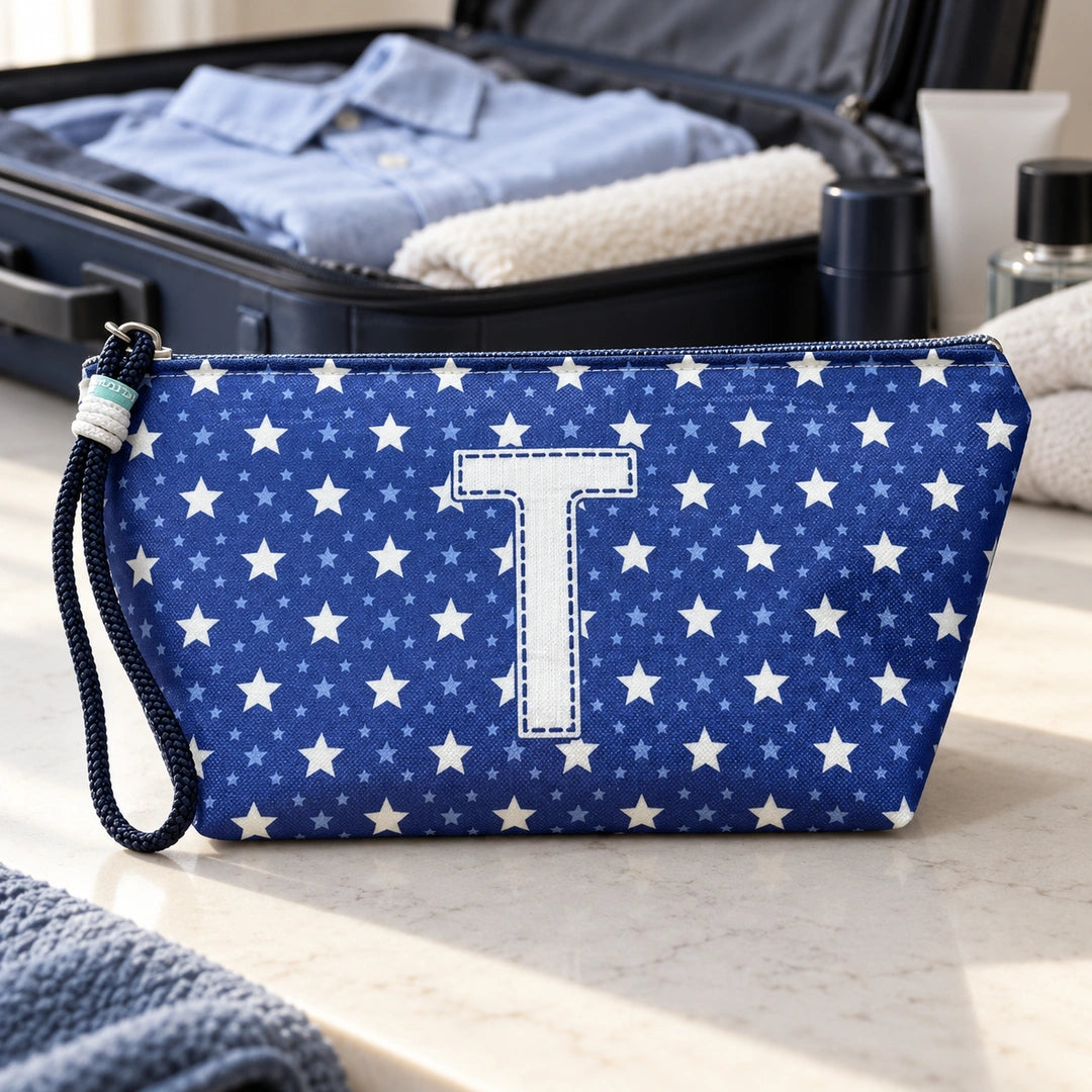 Bolsa Alex azul com letra T fechada num cenário de viagem com mala, roupa e artigos de higiene masculina.