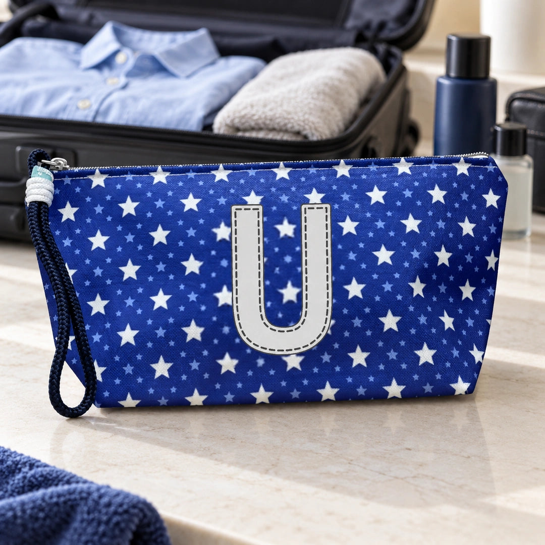 Bolsa Alex azul com letra U fechada num cenário de viagem com mala, roupa e artigos de higiene masculina.
