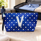 Bolsa Alex azul com letra V fechada num cenário de viagem com mala, roupa e artigos de higiene masculina.