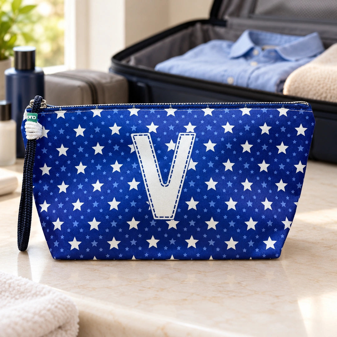 Bolsa Alex azul com letra V fechada num cenário de viagem com mala, roupa e artigos de higiene masculina.