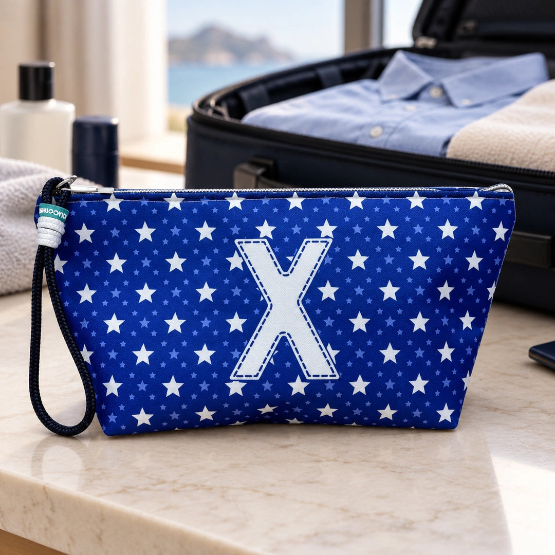 Bolsa Alex azul com letra X fechada num cenário de viagem com mala, roupa e artigos de higiene masculina.