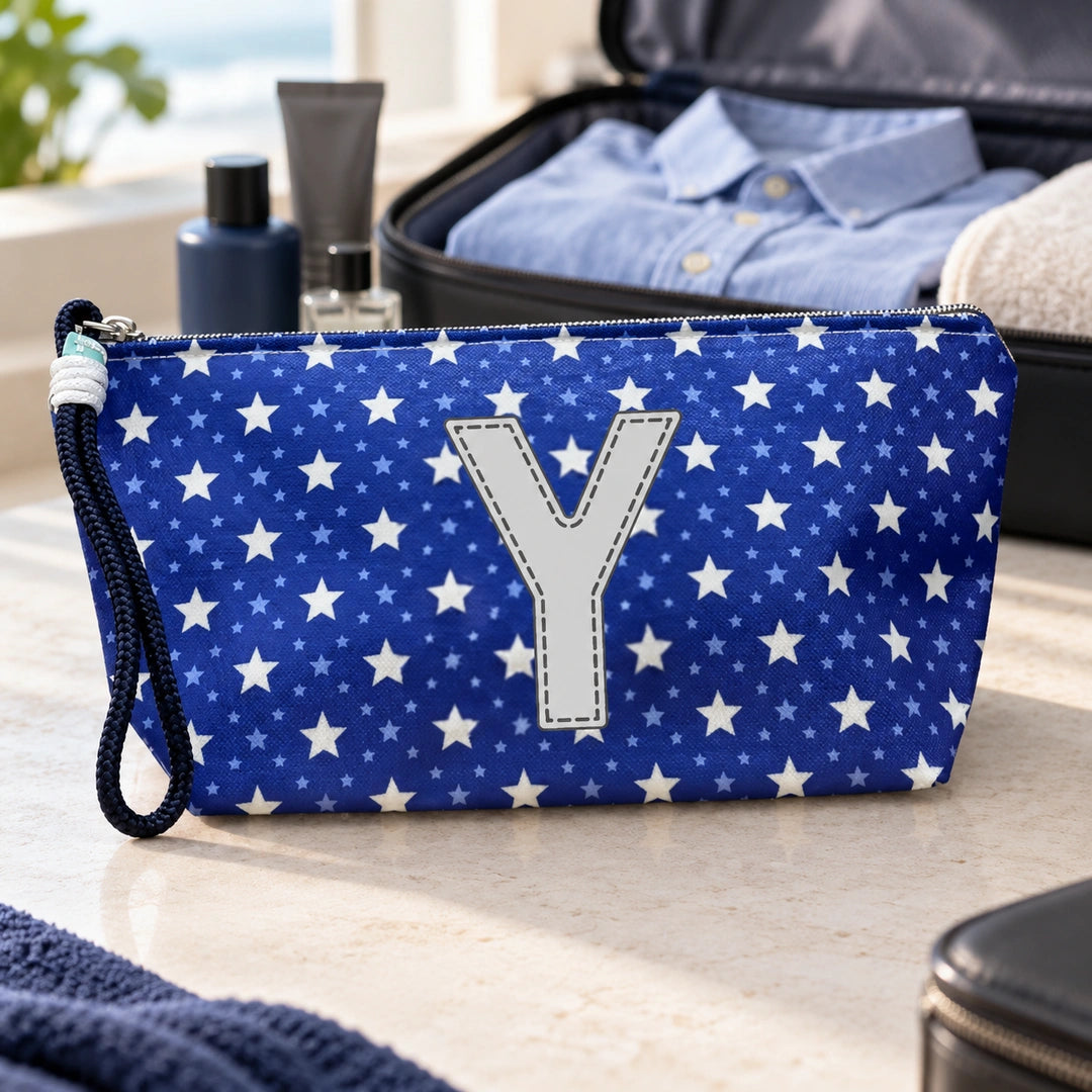 Bolsa Alex azul com letra Y fechada num cenário de viagem com mala, roupa e artigos de higiene masculina.